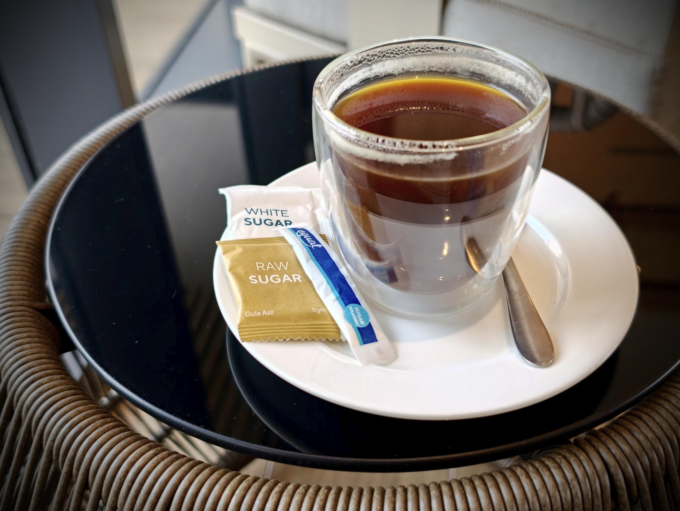 ガラスのカップに入ったブラックコーヒーと、砂糖の小袋