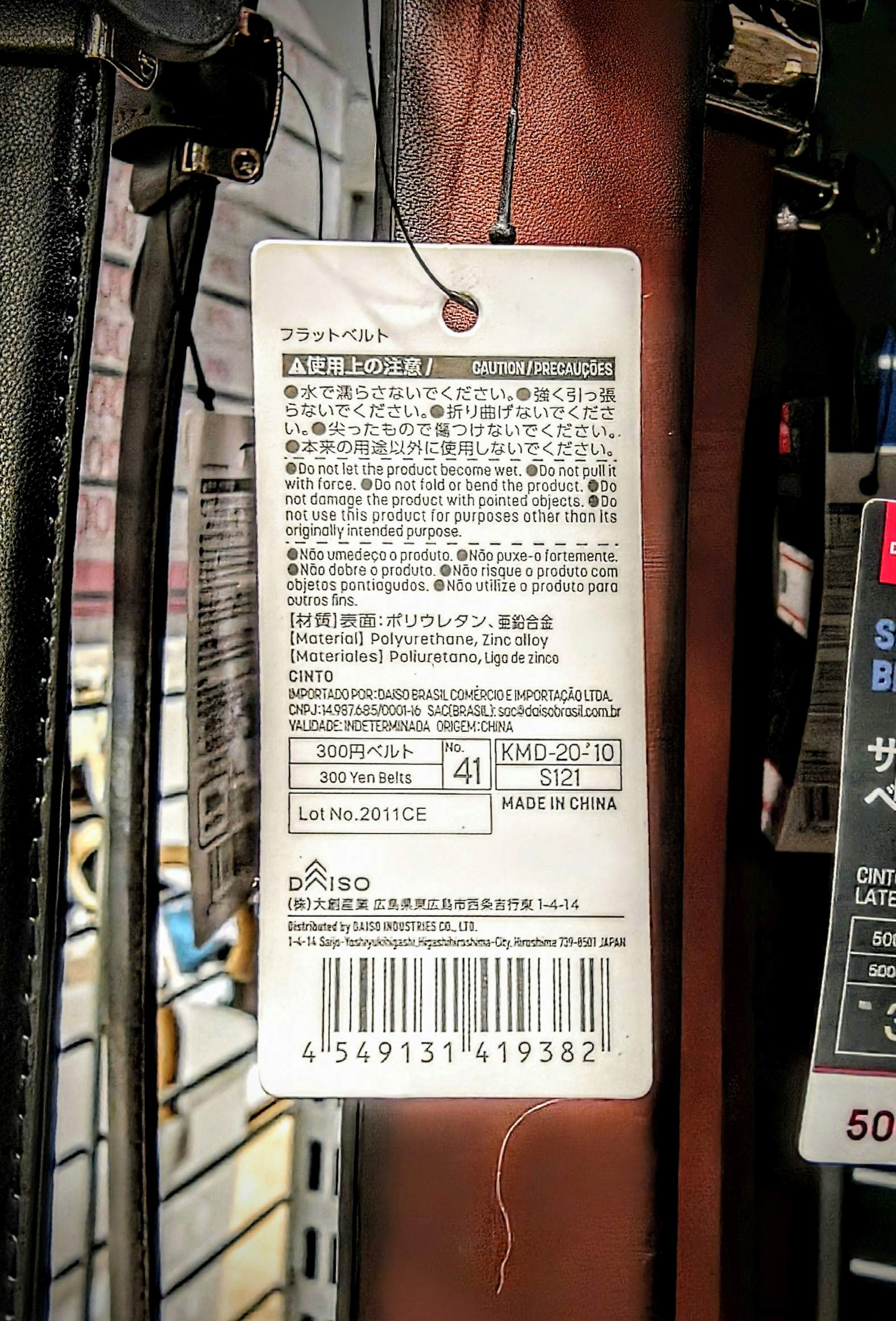 ベルトのタグの裏。日本語、英語、ポルトガル語の注意書きと、DAISO BRASIL の輸入者表示、MADE IN CHINA