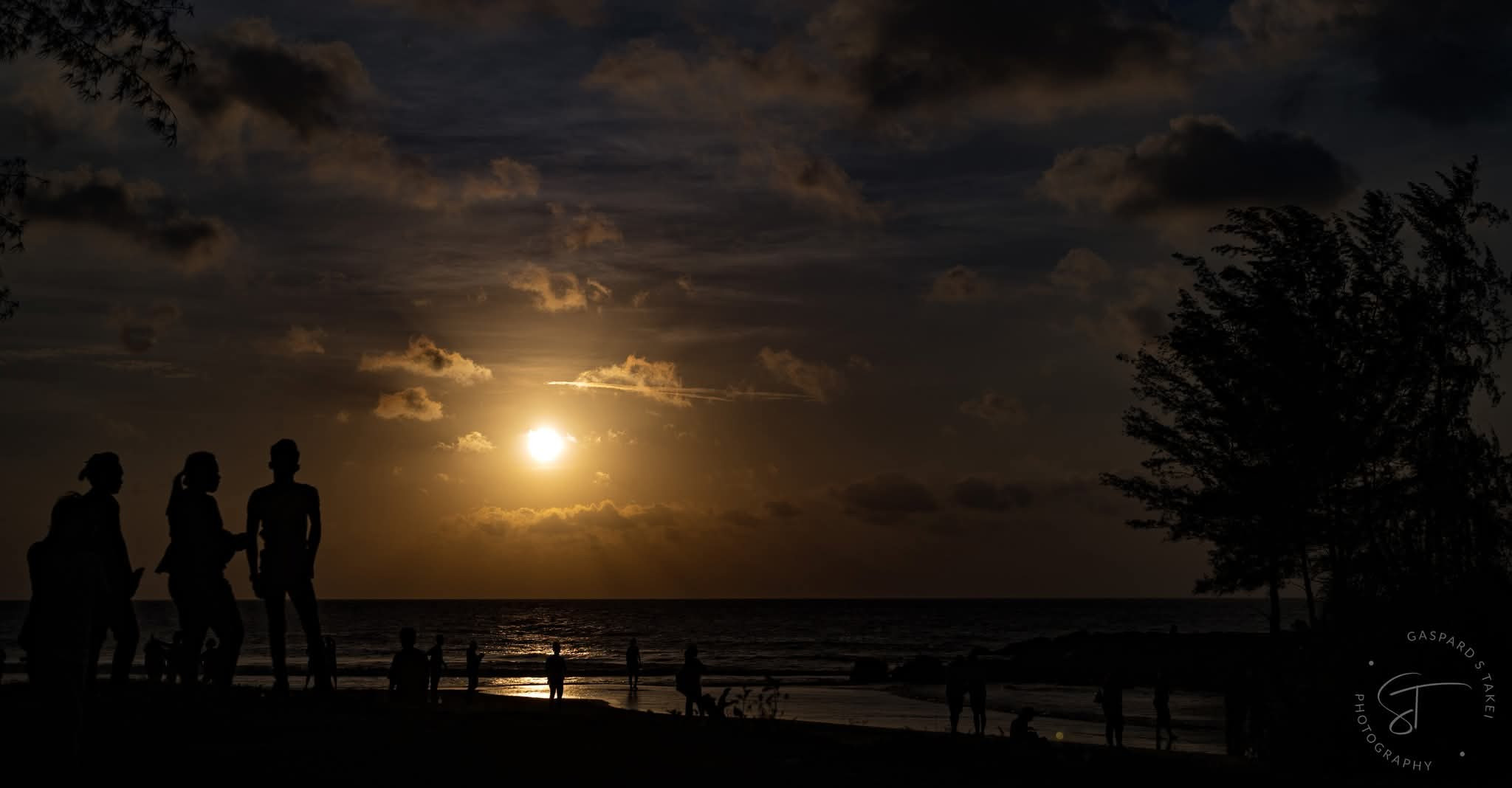 ミリの海に沈む夕日と、海辺に集まる人たちのシルエット
