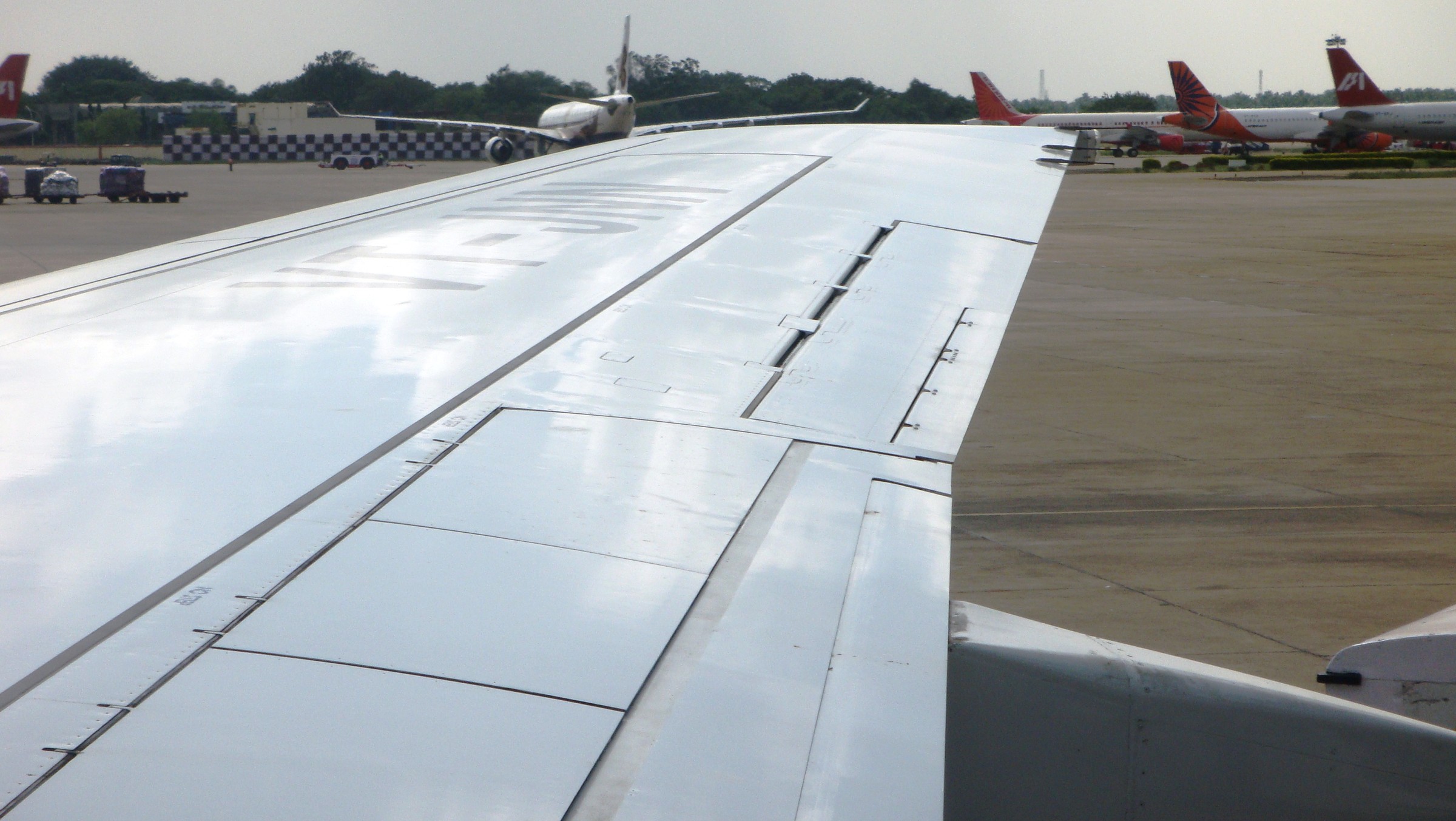 空港の駐機場を背に、窓の外に伸びる旅客機の翼
