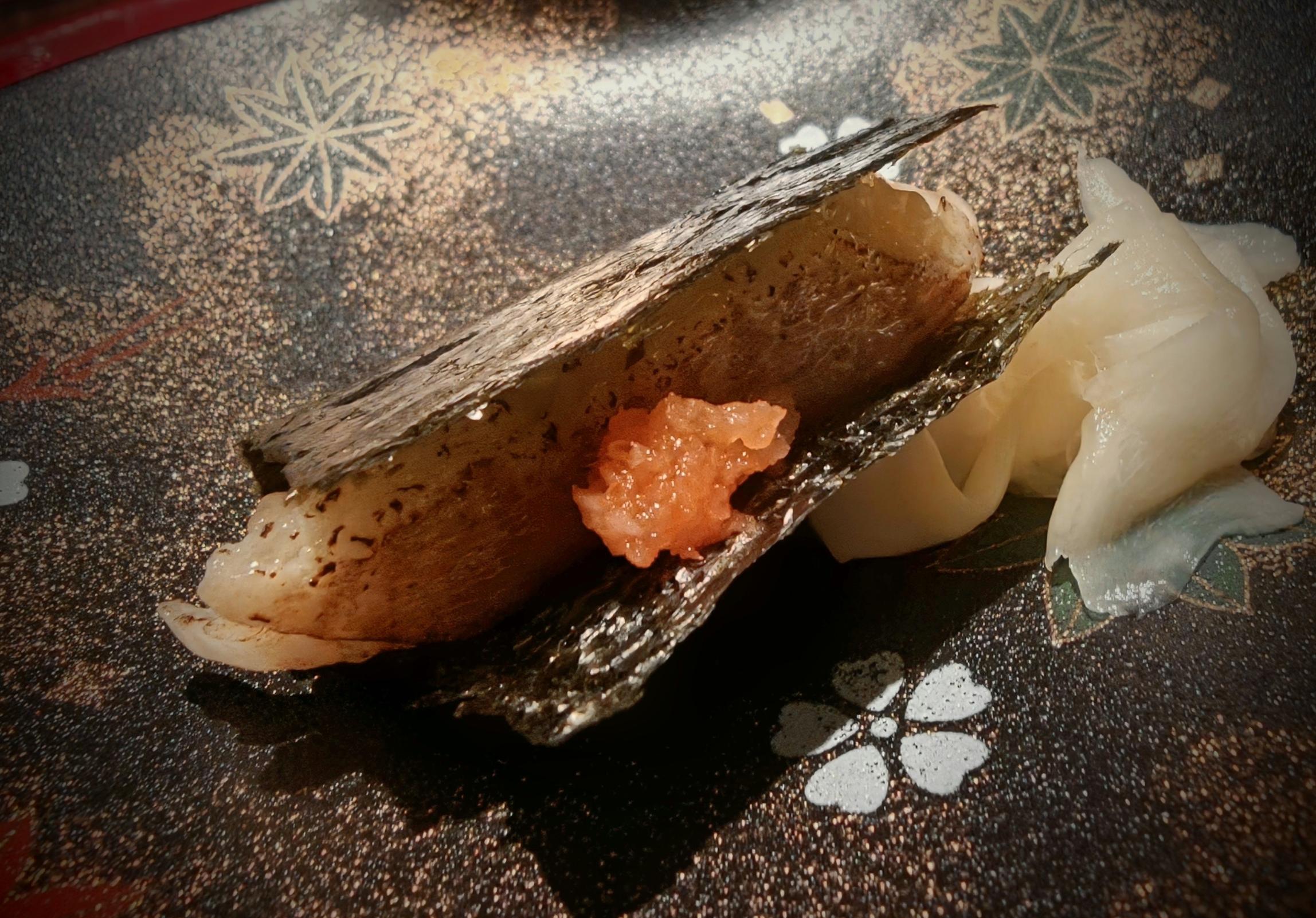 白身の握りを海苔で挟み、橙色の薬味をのせた一貫