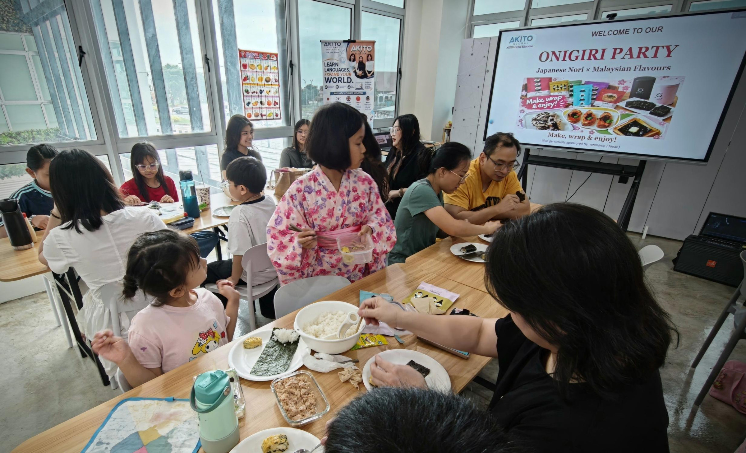 おにぎりパーティーの歓迎スライドの前で、テーブルを囲む参加者と浴衣の女の子
